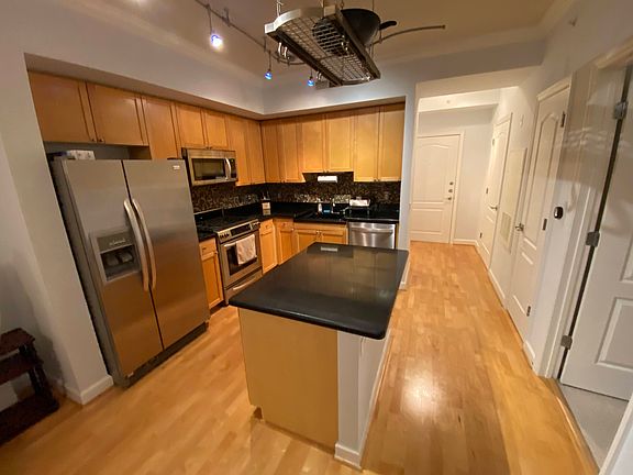 Open concept kitchen with granite countertop island, hanging pot rack, and stainless steel appliances - including a gas stove.