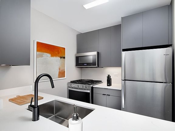 Renovated Package II kitchen with white quartz countertop and backsplash, upgraded stainless steel appliances, upgraded black hardware, and upgraded lighting