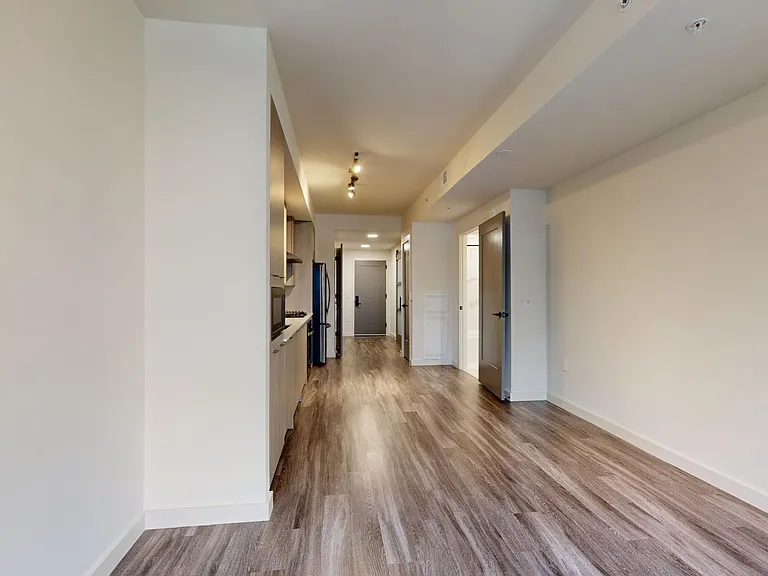 Apartment kitchen with black stainless steel appliances, dining and living room with wood-style flooring.