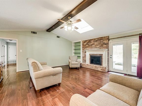 Living room with lofted ceiling with skylight, a fireplace, ceiling fan, and dark wood-type flooring