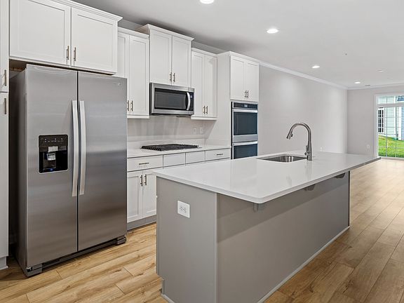 Open kitchen with Upper and Lower White cabinets, gray island and white counters. Opens to living ro