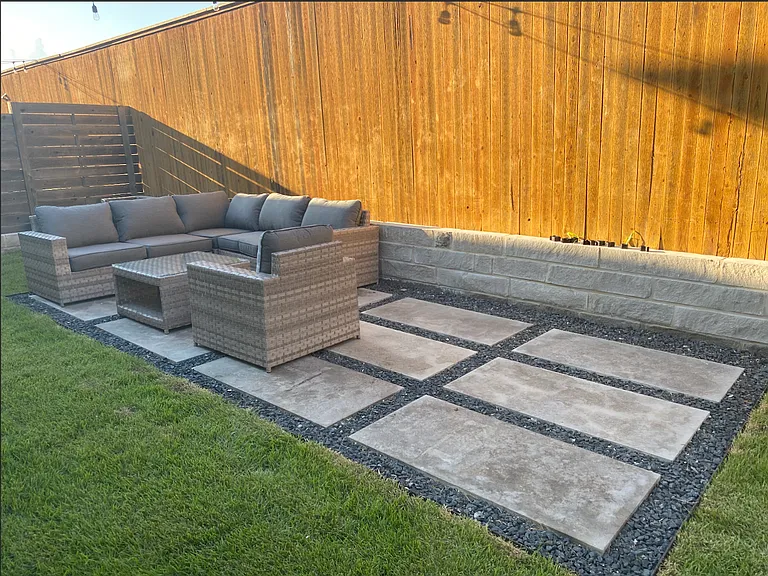 Backyard with paved area, river rock along sides of the house and french drains installed.