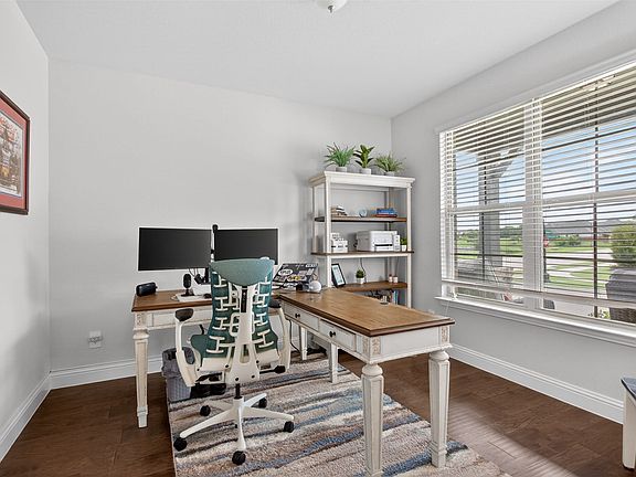 Bright interior room featuring a large window with horizontal blinds, wood-finish flooring, and white walls