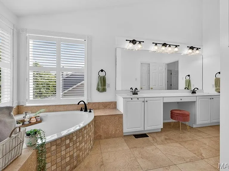 Bathroom featuring a corner soaking tub with tile surround, dual vanity with white cabinetry, integrated makeup area, and wood-finish flooring