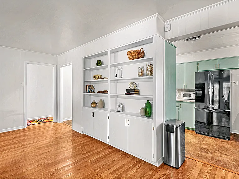 Elegant built-ins showcase stylish decor, adding charm to this open space. The kitchen features mint-green cabinets, modern black appliances, and essentials for your stay. Warm hardwood floors flow throughout, creating a cozy vibe.