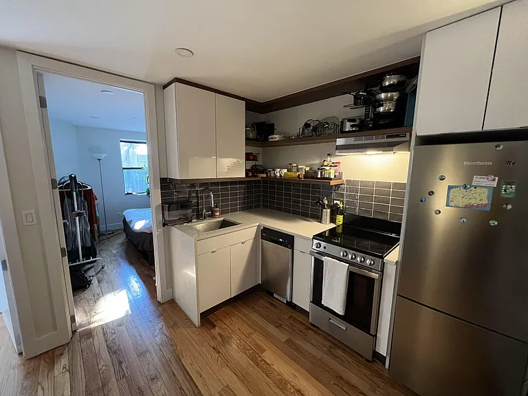 Efficient galley kitchen with ample cabinetry, open shelving, tile backsplash, and stainless steel range, dishwasher, and fri