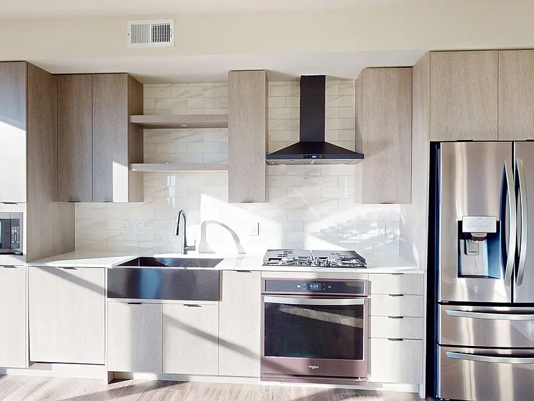 Apartment kitchen with black stainless steel appliances, quartz countertops, wood-style flooring, and custom Italian cabinetry.