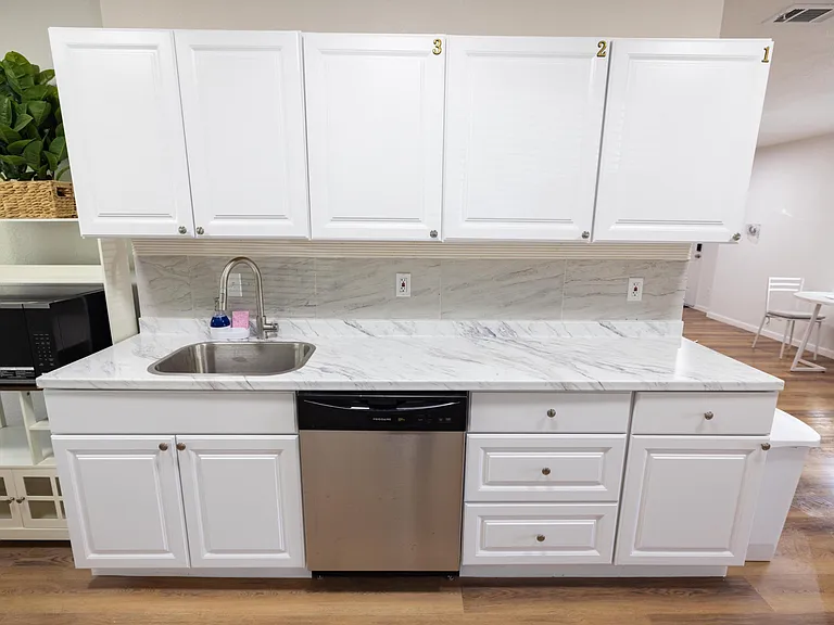 Kitchen counter area with ample white cabinetry, stone-look counters, tile backsplash, and stainless dishwasher.