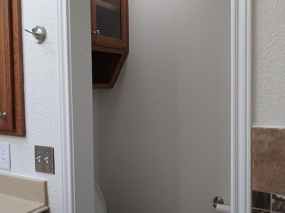 Water closet in master bath with additional storage above toilet. New toilet seat and tissue holder.