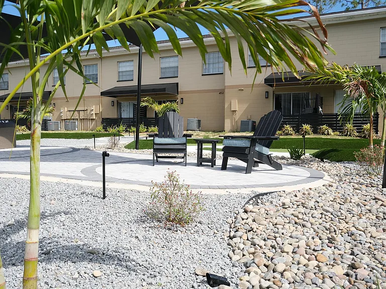 Charming outdoor space with cozy seating area, lush greenery, and modern townhouse backdrop.