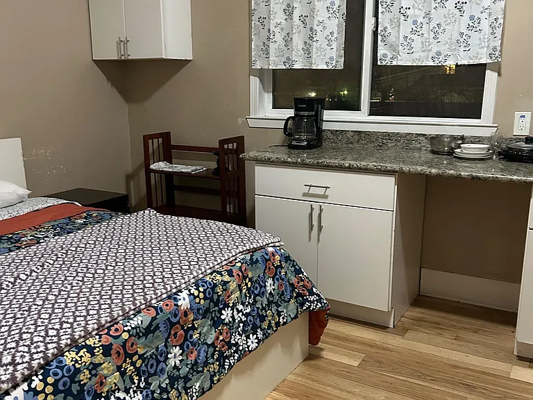 Furnished sleeping area with a bed, cabinet storage, and a counter setup with coffee maker beside a window.