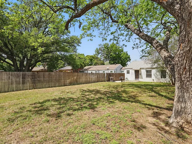 Expansive backyard with a paver patio, established trees providing natural shade, and a storage shed. Grill is non-functioning.