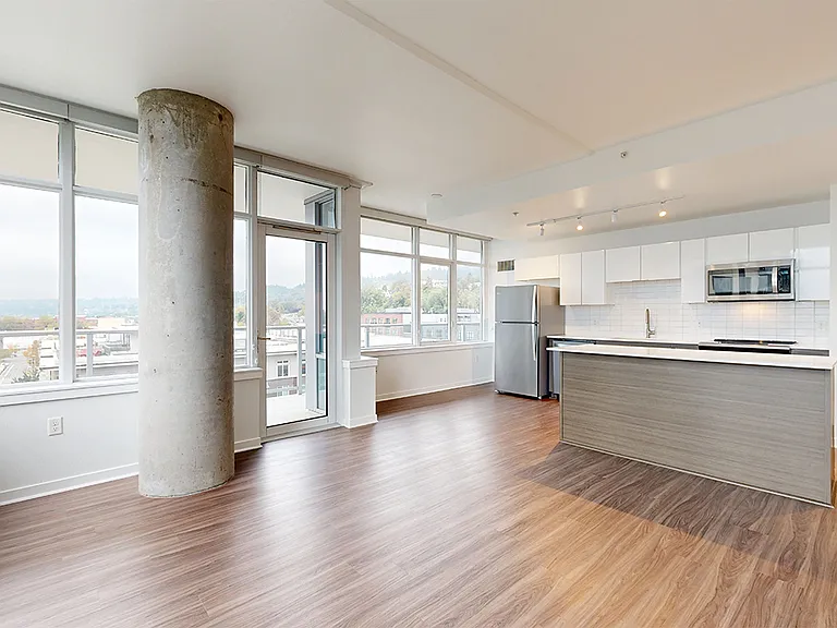 Apartment kitchen with stainless steel appliances, dining and living room with wood-style flooring.