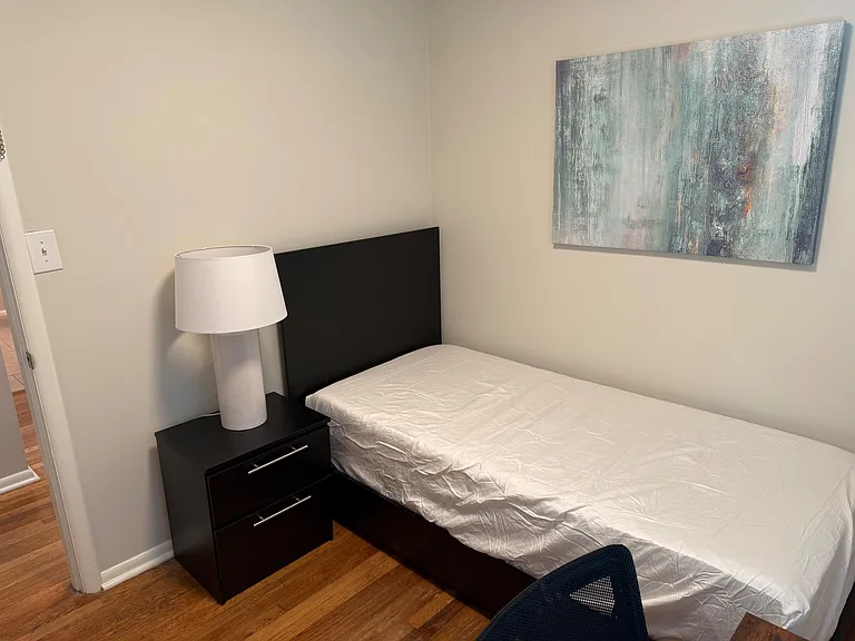 Furnished bedroom with a bed, nightstand and lamp, plus wall art and durable flooring for easy upkeep.