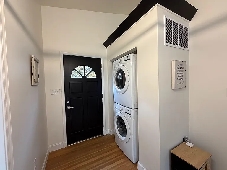 Dedicated entry/laundry nook with stacked front-load washer/dryer, hardwood floors, and a nearby coat/utility area.