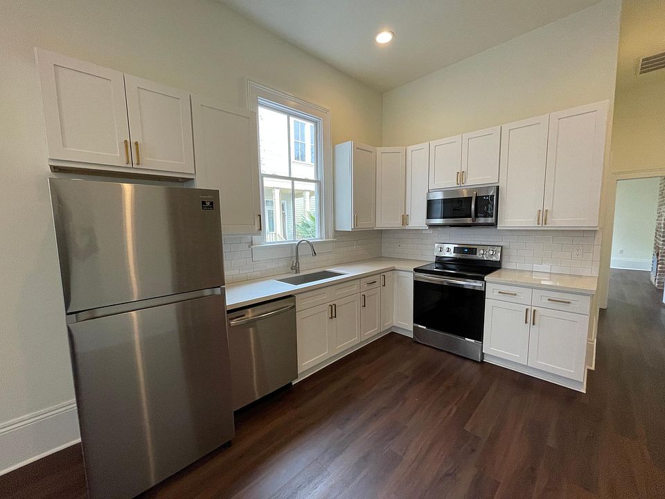 White shaker kitchen cabinets with brass hardware, soft close doors, and drawers. Deep stainless steel sink with sprayer. Samsung stainless steel fridge, glass top electric stove, microwave, and dishwasher.