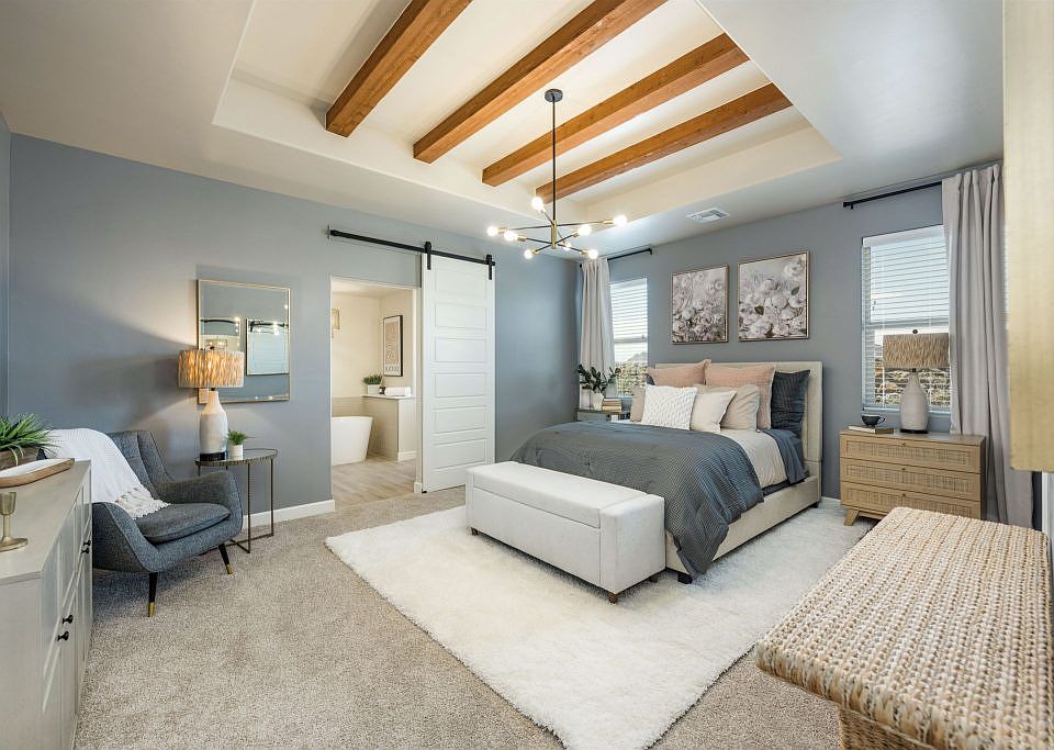 A modern bedroom with gray walls, carpeted floor, and wooden ceiling beams. Features a bed with gray