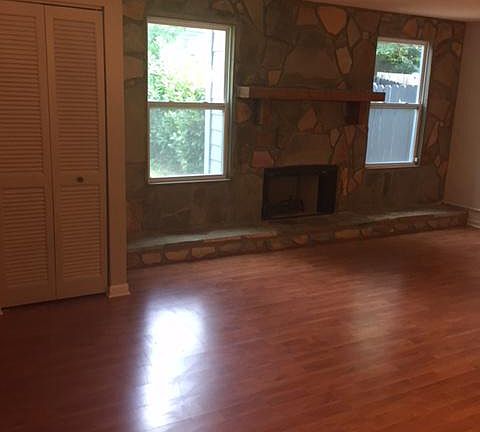 Living room with stone wall fireplace. Two tall windows look into private backyard.