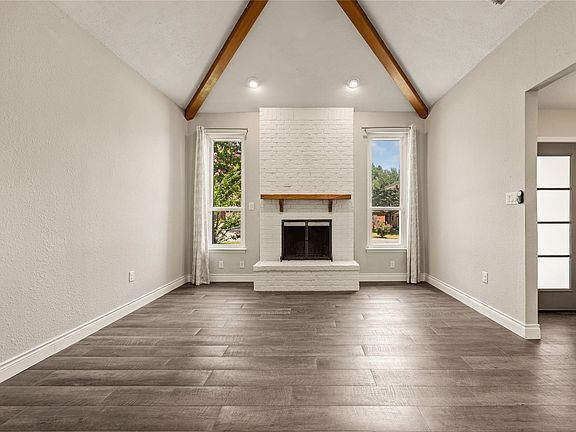 Vaulted ceiling with exposed wood beams, white painted brick fireplace with wood mantel, wood-finish flooring, and recessed lighting