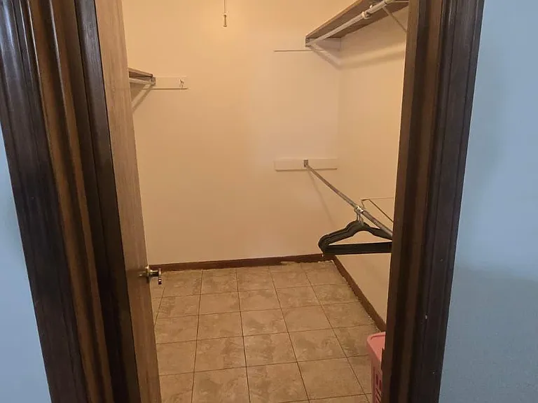 Large walk-in closet with tiled flooring and built-in hanging rods and shelving for organized storage.