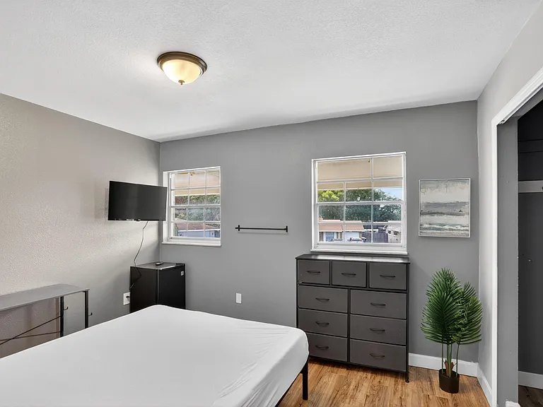 Bedroom with two windows, wood-look flooring, a dresser for storage, and space for a bed and small desk area.