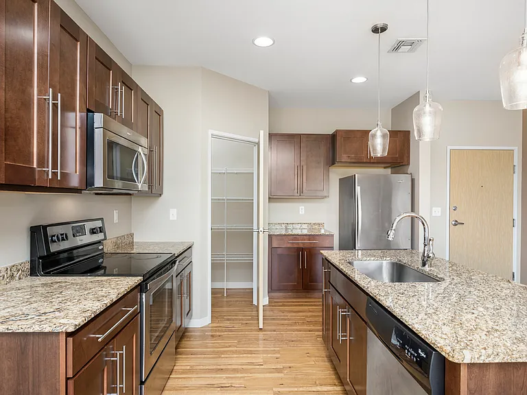 Modern kitchen with sleek dark wood cabinets, granite countertops, and stainless steel appliances. Spacious layout with elegant pendant lighting and ample pantry space. Modern kitchen with sleek dark wood cabinets, granite countertops, and stainless steel