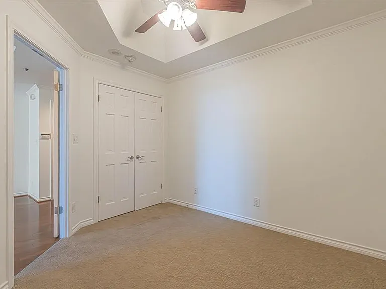 Carpeted room featuring a ceiling fan, tray ceiling, crown molding, and bifold closet doors