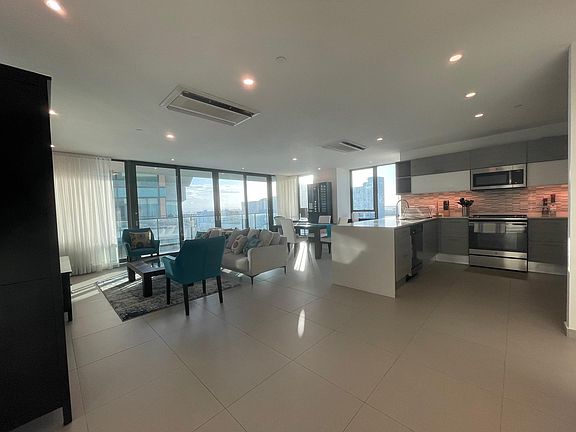 Open living, dining, and kitchen area featuring panoramic floor to ceiling glass doors and windows.