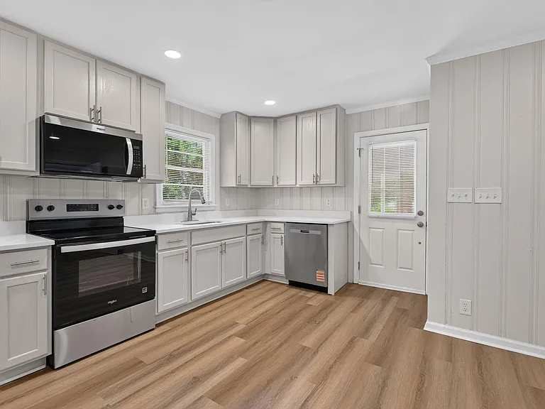 Efficient L-shaped kitchen with ample cabinet storage, stainless appliances, and a windowed sink plus exterior door access.