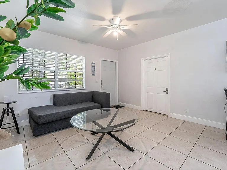 Open living area with tiled floors, a large window with blinds, and a ceiling fan for comfort and airflow.