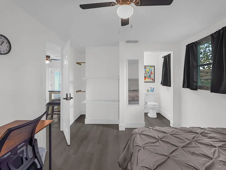 Private bedroom with work desk, ceiling fan, window with blackout curtains, and open shelving for added storage.