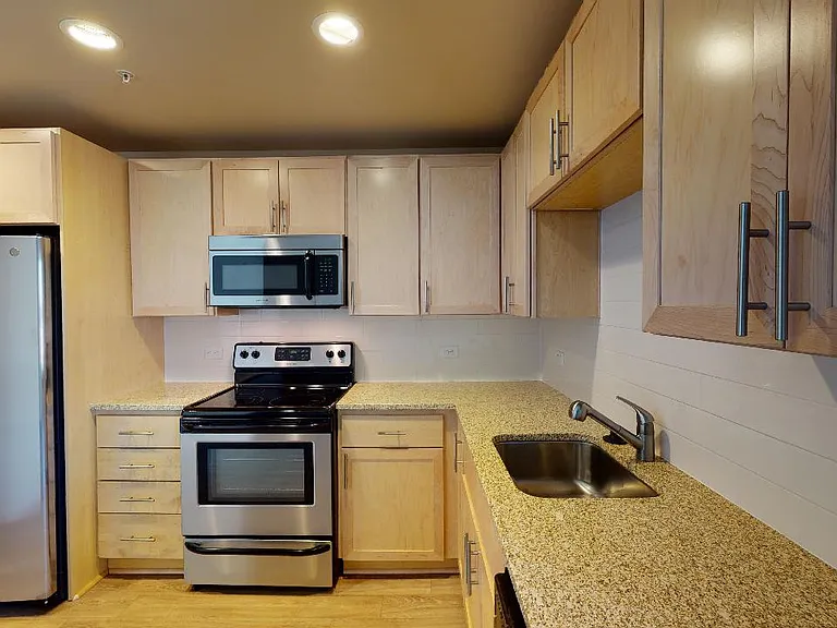 Apartment kitchen with stainless steel appliances, granite countertops and wood-style flooring.