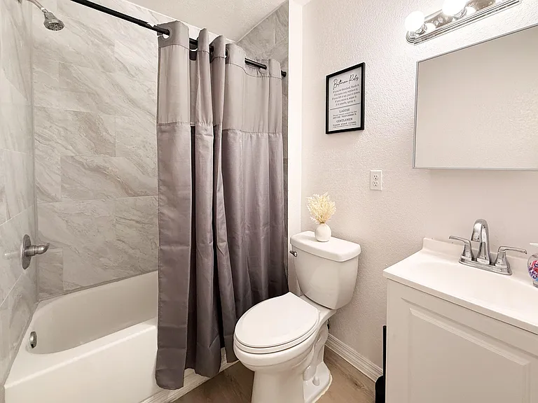 Clean full bath with tub/shower combo, tile surround, and vanity with mirror and overhead lighting for daily routines.