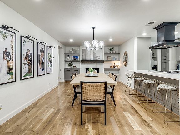Open-concept dining area featuring wood-finish flooring, a contemporary chandelier, and a built-in fireplace with a wood mantle