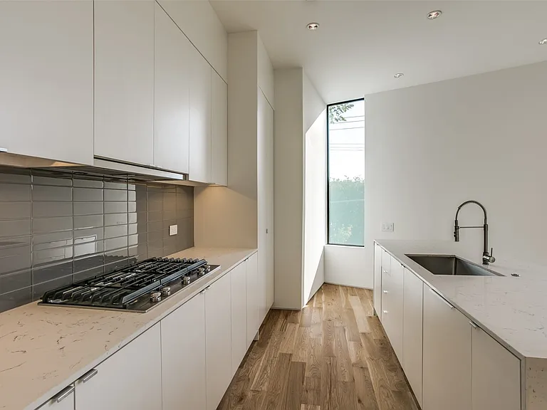 Contemporary kitchen featuring a gas range, slab cabinetry, light-toned countertops, a stainless steel sink with a gooseneck faucet, and wood-finish flooring