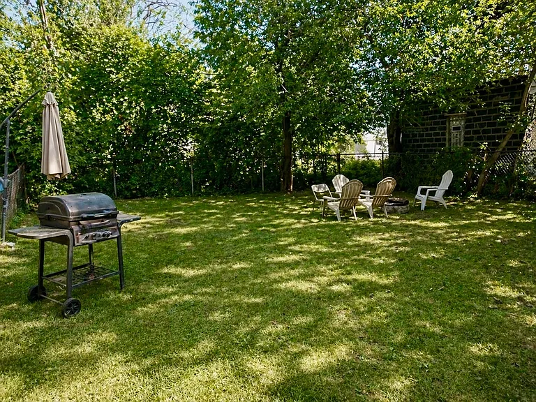 Spacious backyard featuring a lush green lawn and natural shade, ideal for relaxing outdoors or entertaining guests. Includes a barbecue area, perfect for weekend grilling and gatherings, with plenty of room for outdoor seating, play, or gardening.