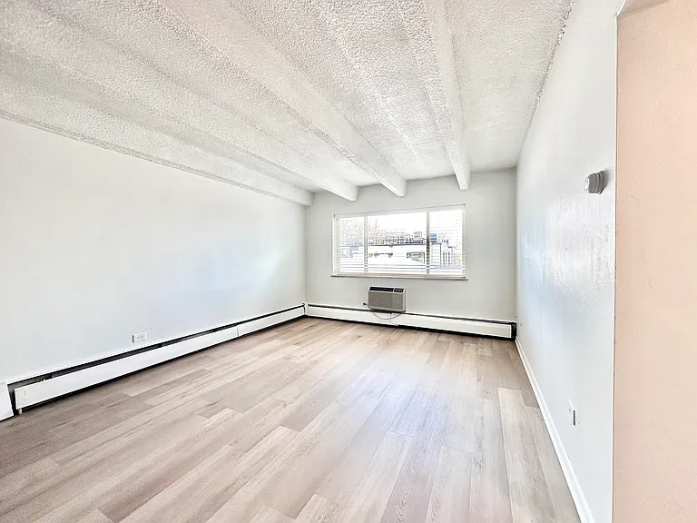 Bright and airy living space with large window, wood flooring, and modern baseboard heating. Bright and airy living space with large window, wood flooring, and modern baseboard heating.
