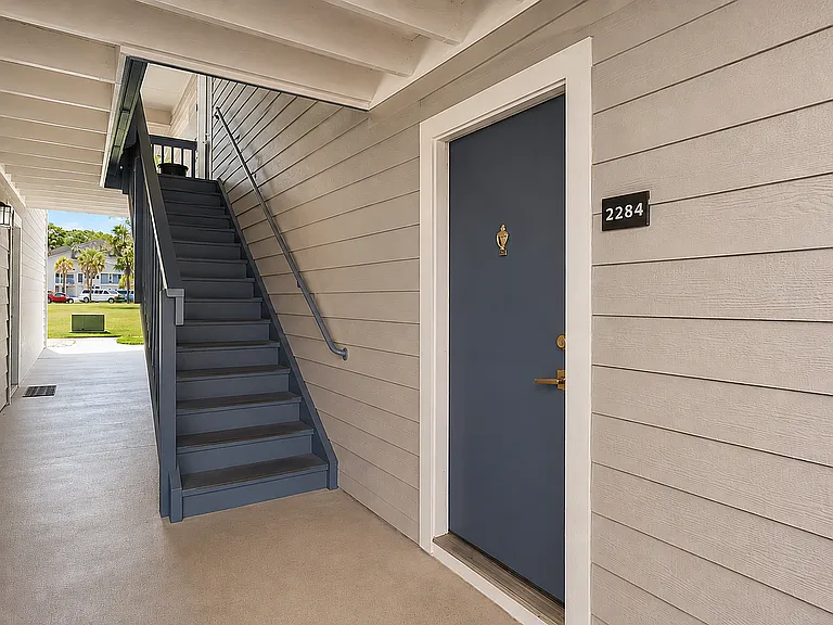 Inviting apartment entrance with stylish blue door and sunny outdoor stairs, showcasing modern charm and convenient access.