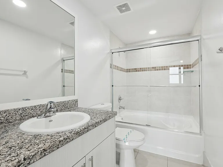 Bathroom featuring a glass-enclosed tub with a granite countertop vanity