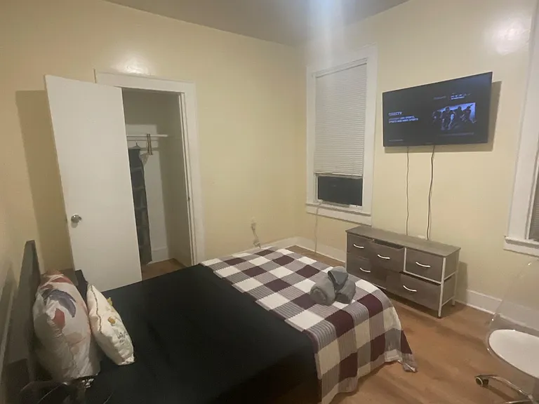Furnished bedroom featuring a bed, dresser, wall-mounted TV, and a closet for everyday storage needs.