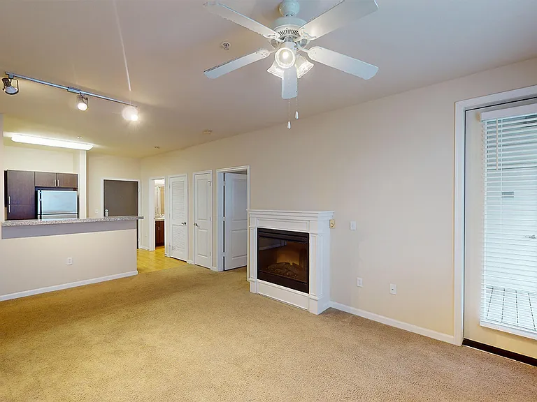 Apartment kitchen with stainless steel appliances, dining and living room with plush carpet flooring.
