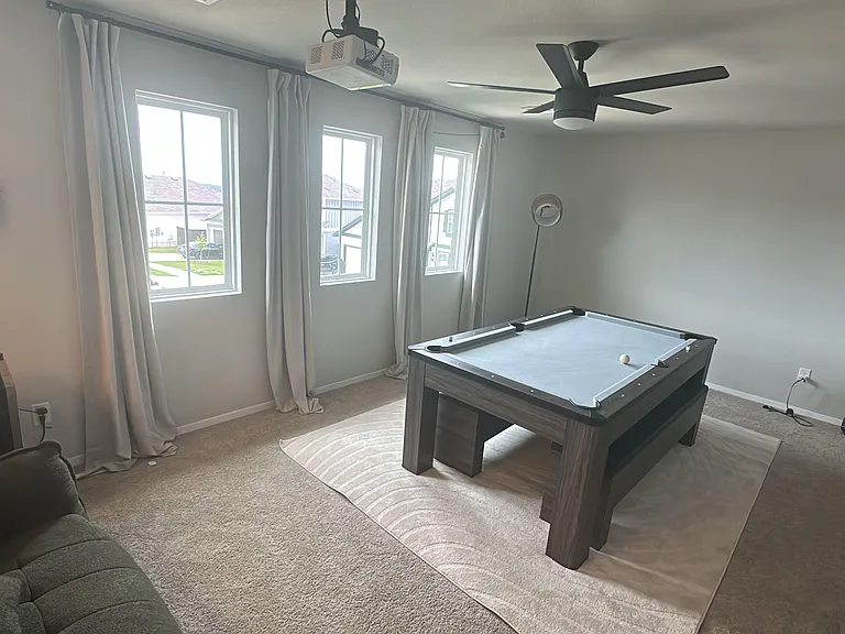 Carpeted bonus room with three large windows, ceiling fan, and plenty of floor space for recreation or lounging.