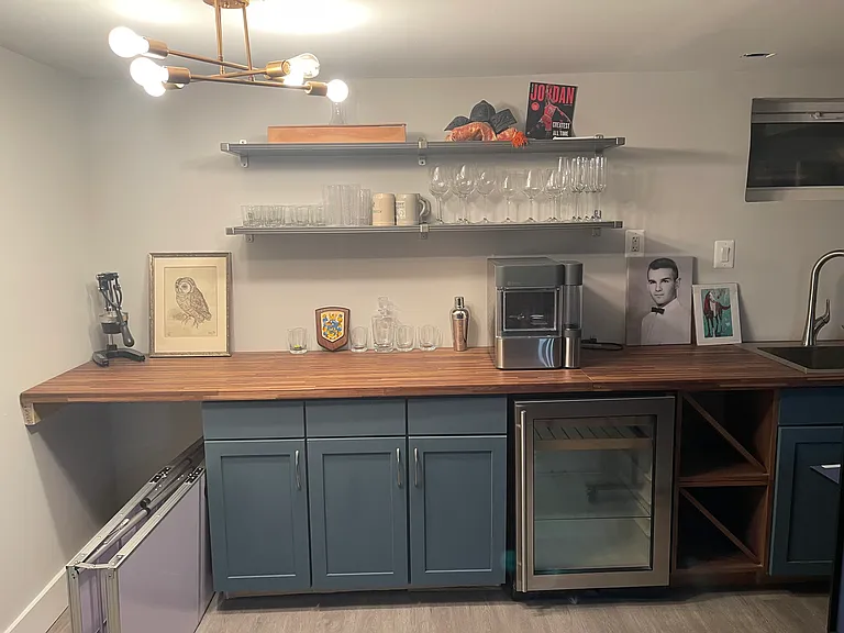 A true entertainer's dream, this custom wet bar features designer blue cabinetry, butcher block countertops, a built-in wine chiller, dishwasher, open shelving, and dedicated wine storage, bringing style and function together for unforgettable gatherings.