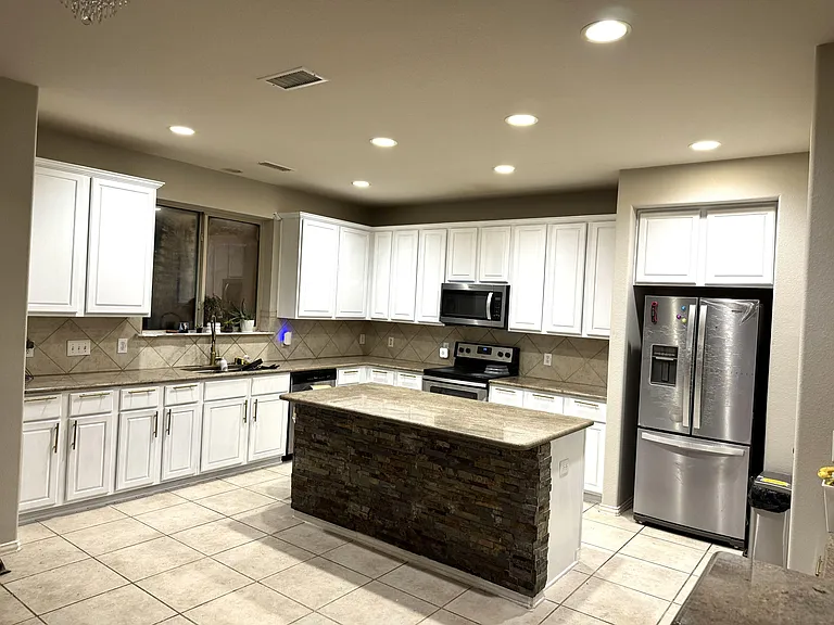 Spacious kitchen with ample white cabinetry, center island, tile backsplash, and stainless steel appliances for daily cooking
