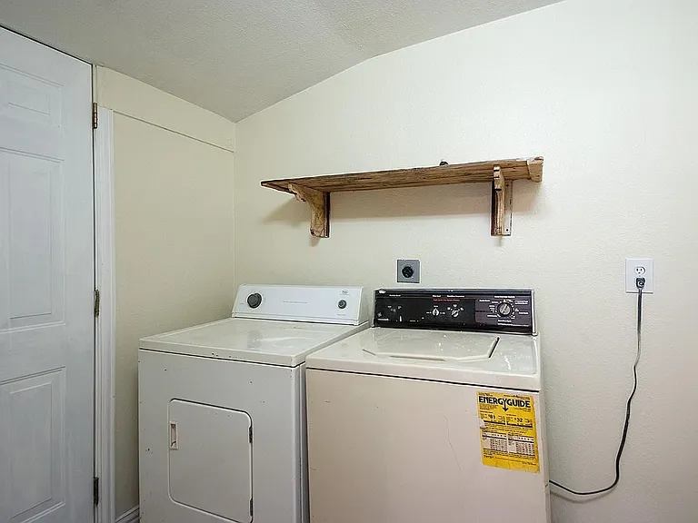 Utility room with a side-by-side washer and dryer, neatly arranged with a shelf above for storage.