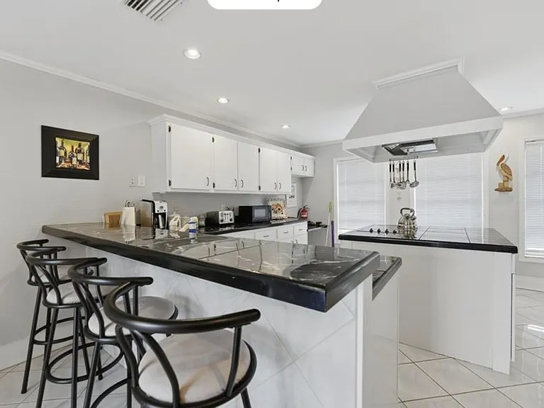 Spacious kitchen with long breakfast bar seating, ample cabinetry, and a wide cooktop area with vent hood.