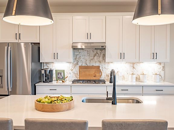 Kitchen with large island, pantry, appliances, white cabinetry and accent patterned backsplash and g