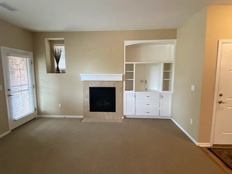 Living room with gas fireplace and bookcase with storage. Patio door is visible on the left, also with a security door.