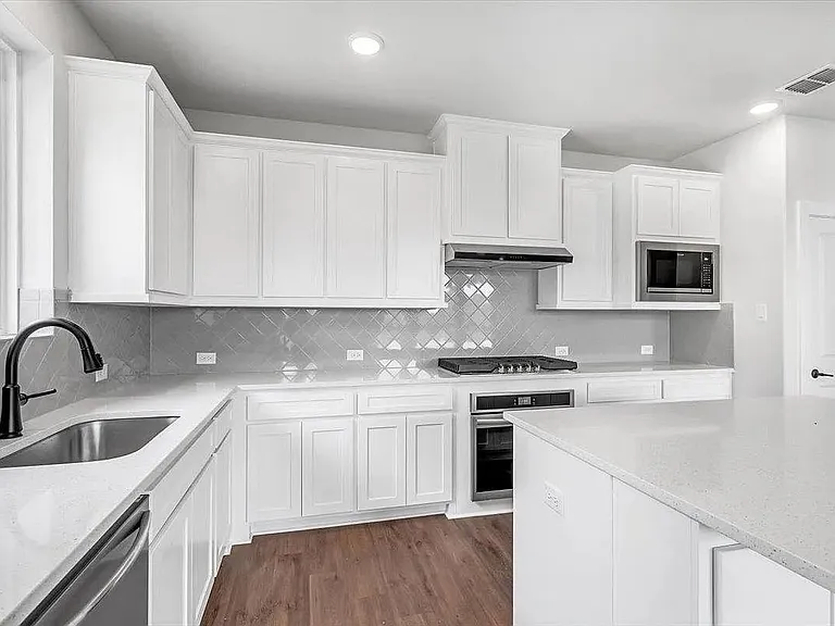 Contemporary kitchen featuring white cabinetry, light-toned countertops, stainless steel appliances, and a gray geometric tile backsplash