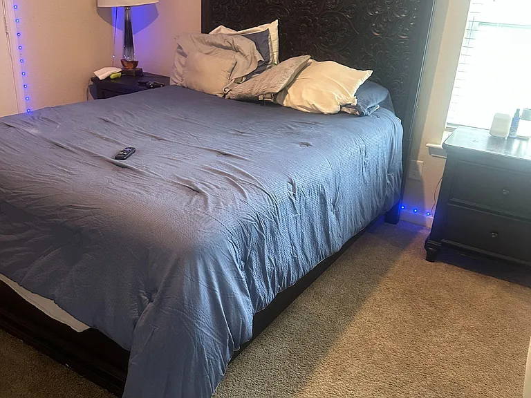 Furnished bedroom featuring a large bed with an ornate headboard, nightstands, and a window with blinds for natural light.